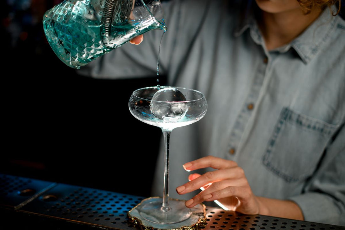 Un bartender met un glaçon rond transparent dans un verre à cocktail